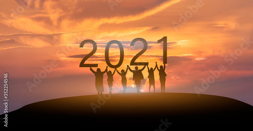 Happy new year 2021, Silhouette of 2021 letters on the mountain with business people raised arms in teamwork concept at sunrise.