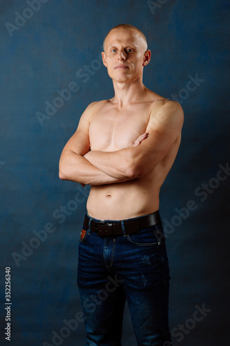 Portrait of strong healthy handsome Athletic Man Fitness Model wearing jeans posing near dark blue wall