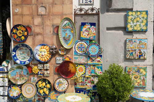 Vietri/Italy - 09.30.2018: Outside of a colorful souvenir store selling traditional handcrafted ceramics in vivid colors. Amazing designed tiles and plate pottery gifts hanging on a wall