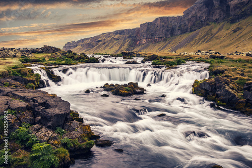 Typical Icelandic nature landscape. powerful glacier river with waterfall and old Volcanic mount with colorful sky during sunset. Fantastic Iceland nature