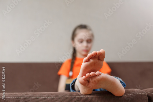 A little caucasian girl with bare feet reading book while sitting on a sofa at home. Foot closeup. selective focus