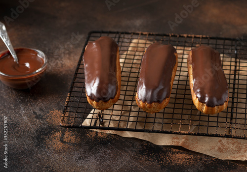 homemade eclairs with cream and chocolate icing on a dark concrete background. chocolate dessert. horizontal image.