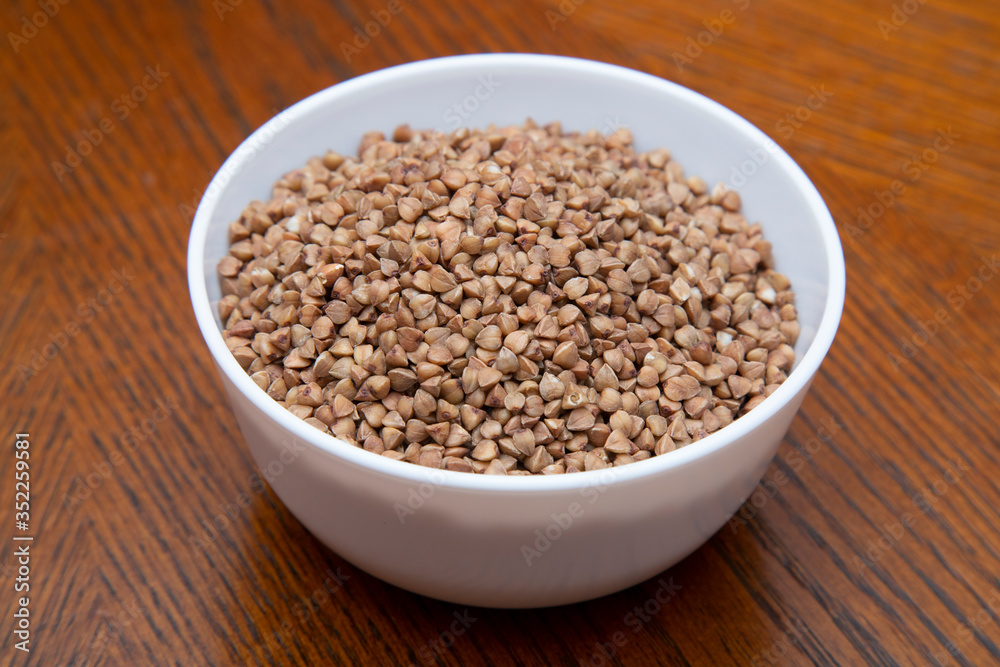Buckwheat in a white Cup on a brown table. Buckwheat in a white Cup on a brown table.