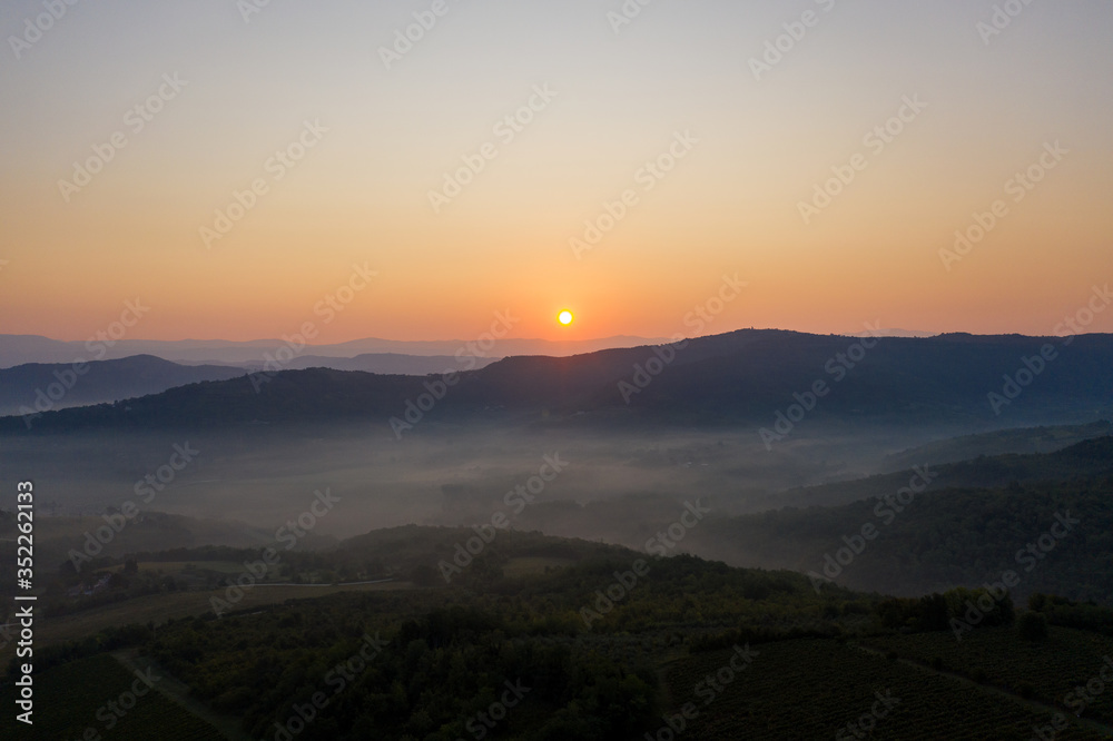 Sunrise in a mountainous area. The valley between the mountains is filled with fog. Shooting from a drone.