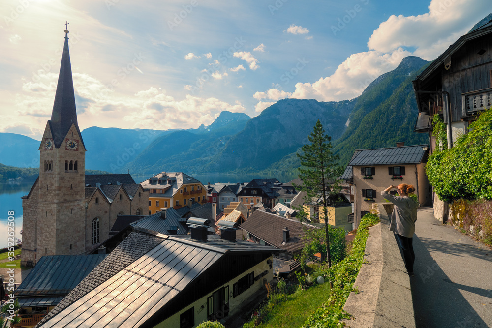 Obraz premium Female tourist looking at stunning Hallstatt, Salzkammergut region, OÖ, Austria, from an elevated viewing point above the roofs of the famous village