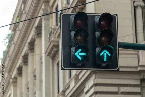 An automated traffic light in the city turned green. Arrow signs are showing straight and left directions to go ahead and move on.
