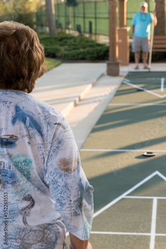 A retired couple playing a game of shuffleboard on an outdoor court photo