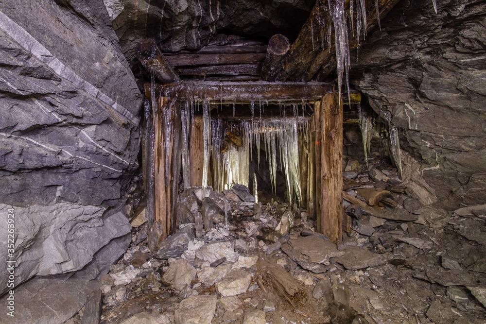 Underground old mica mine tunnel with collapsed wooden timbering and ice stalactites stalagmites