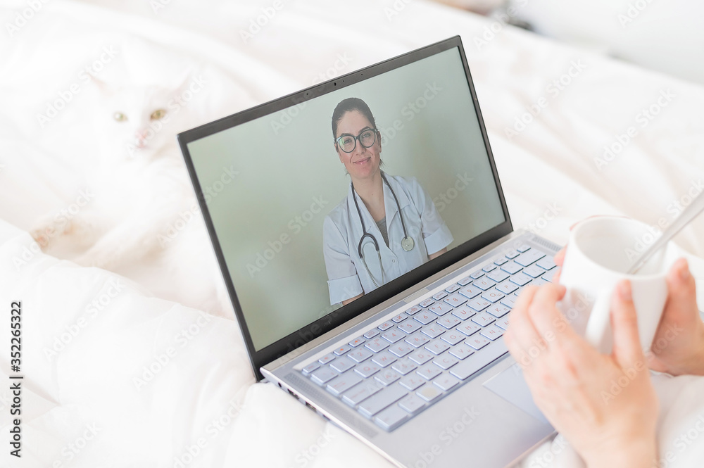 A faceless woman drinks an antipyretic and watches a video from a doctor recommendation. Online doctor consultation on a webcam without leaving your home. The cat lies in bed with a sick housewife. A faceless woman drinks an antipyretic and watches a video from a doctor recommendation. Online doctor consultation on a webcam without leaving your home. The cat lies in bed with a sick housewife.