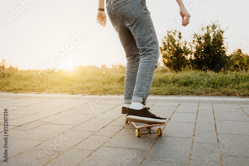 Skater von hinten mit Jeans fährt auf Skateboard im Sommer bei Sonnenuntergang mit Natur im Hintergrund