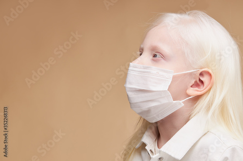 coronavirus, covid-19 concept. little unusual albino child in medical mask isolated, sick kid suffer from emidemic covid-19, protect herself with the use of mask photo