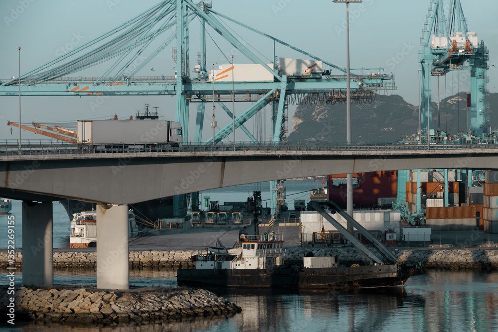 Sea transport and land transport. Activity in the commercial dock of Algeciras, Spain, with trucks and ships loading and unloading containers. In the background you can see the Rock of Gibraltar.