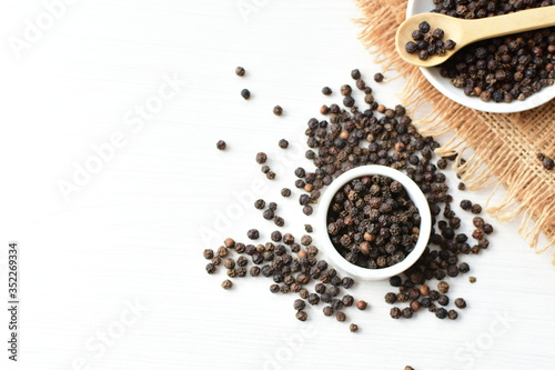 Black peppercorns in bowls on white wooden background