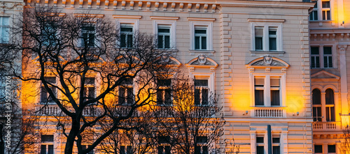 European illuminated facade near some trees without leaves in the evening.