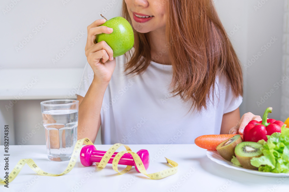 Women hand holding green apple with fruits, vegetables, water, dumbbell and tape measure on white table background. Selection of healthy food. Organic food, diet, lose weight concept. Close up Women hand holding green apple with fruits, vegetables, water, dumbbell and tape measure on white table background. Selection of healthy food. Organic food, diet, lose weight concept. Close up