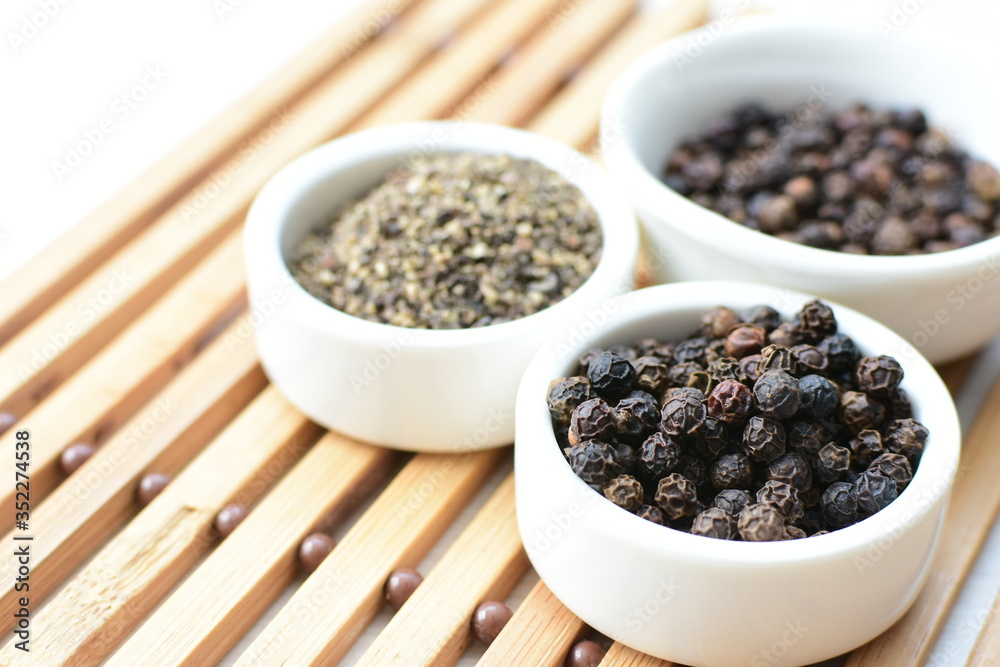 Black peppercorns in bowls on white wooden background