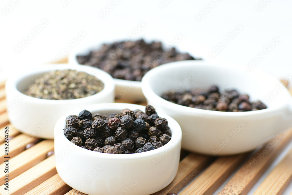 Black peppercorns in bowls on white wooden background Black peppercorns in bowls on white wooden background