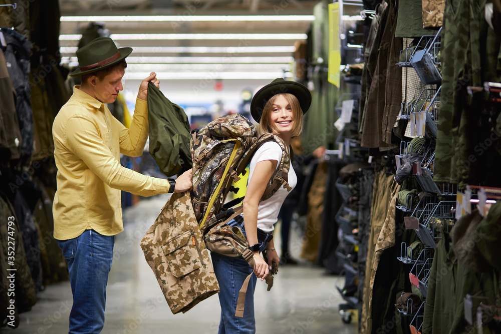 beautiful married couple going to go in mountains, shopping together in sportive wear store, handsome guy and beautiful woman try on green wear and bags