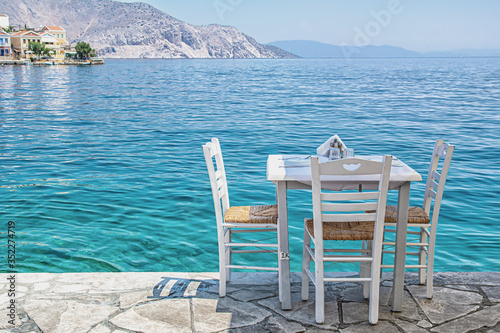 Chairs with tables in typical Greek tavern near the sea in Symi town
