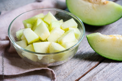Cut of fresh sweet green melon in bowl glass on the wooden background. Fruits or healthcare concept. Selective focus, close up