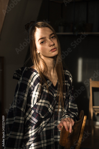 the girl sits on a chair in a plaid shirt, put her hands on the back of the chair, the ray of the sonde falls on her face © Maxim