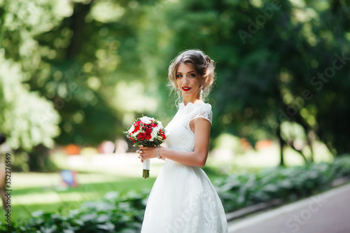 brunette bride in a dress with a wedding bouquet in the park on a background of greenery