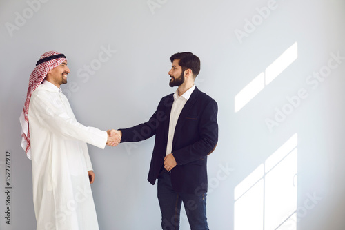 Handshake of arabic and european businesspeople in gray background office.