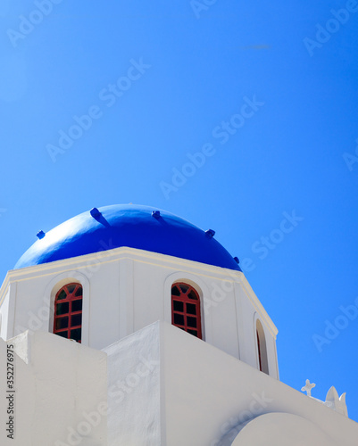 White church with blue dome against blue sky background. Santorini, Greece.