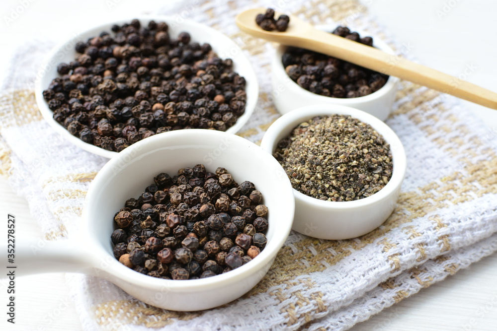 Whole and ground black peppercorns on white wooden background Whole and ground black peppercorns on white wooden background