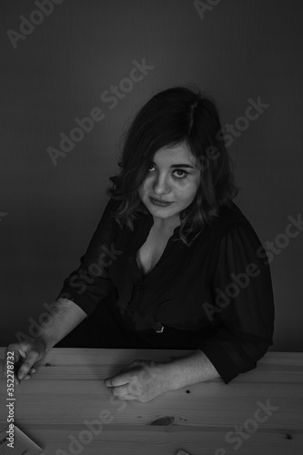 a girl of Georgian appearance sits at a table crying, a girl with curly hair flows a tear on her cheek, sits sad at a table