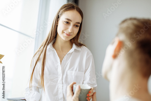 cute caucasian lady nicely talk with husband in the morning. woman smile and look at man with love while he is sitting on chair. family, relationships concept