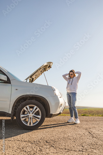 woman standing near car with opened hood on sunset