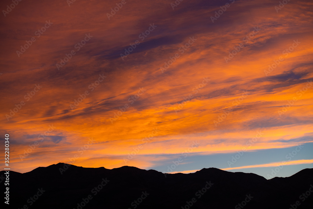 A stunning sunset or sunrise scene of silhouette mountain peaks and purple ridges with the twilight background, the blue sky and the pink-yellow skyline