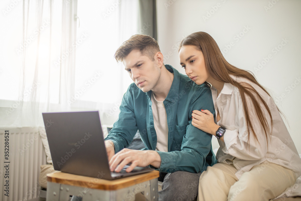 young caucasian lady always next to her husband working at home with laptop. woman talk to man, try to entertain and support him. family, freelance concept young caucasian lady always next to her husband working at home with laptop. woman talk to man, try to entertain and support him. family, freelance concept