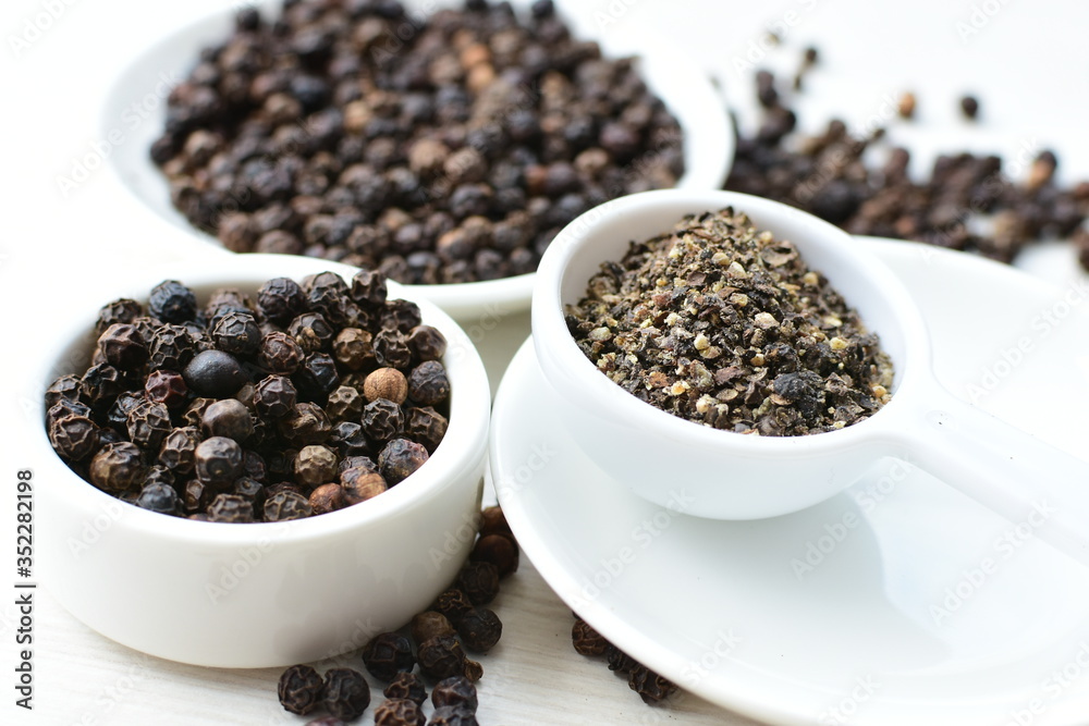 Whole and ground black peppercorns on white wooden background Whole and ground black peppercorns on white wooden background