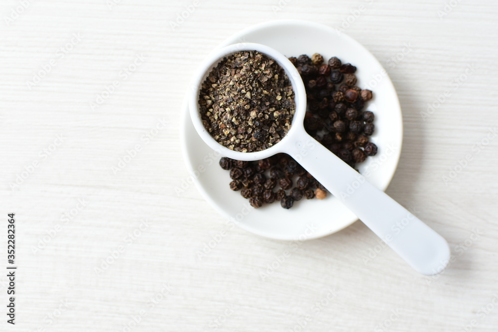 Whole and ground black peppercorns on white wooden background Whole and ground black peppercorns on white wooden background