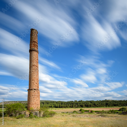 Vieja chimenea de ladrillo rojo bajo un cielo azul con nubes blancas photo