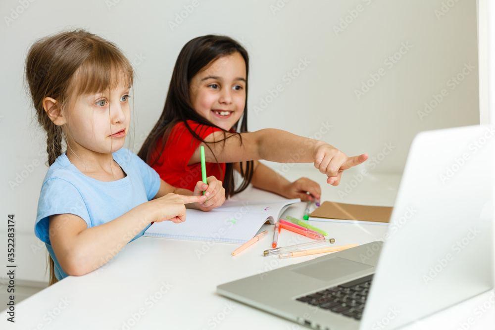 Two girls, the oldest and the youngest, are engaged at a table on a laptop. Two girls, the oldest and the youngest, are engaged at a table on a laptop.