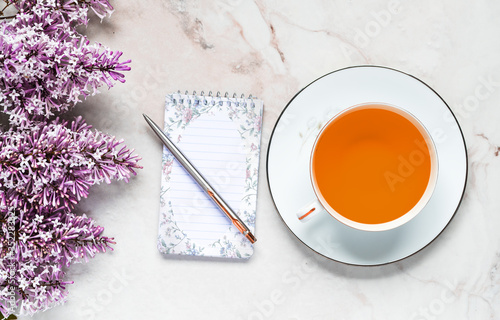 фотографія Lilac Flowers with cup of tea and note pad pen on Marble