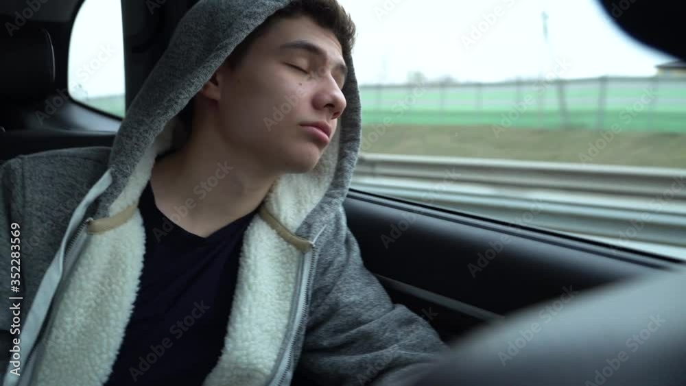 The teenager is texting on the phone in the back seat of the car, then turns away and looks out the window. The camera is shaking slightly