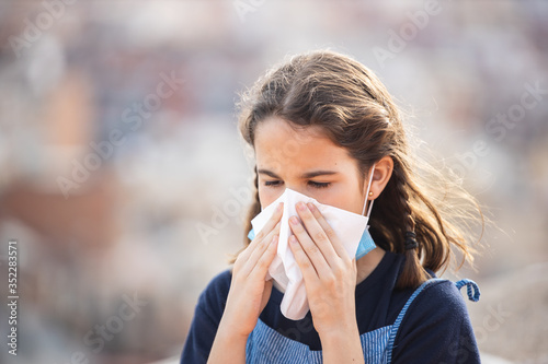 Sick little girl with allergy sneezing with a handkerchief in the city