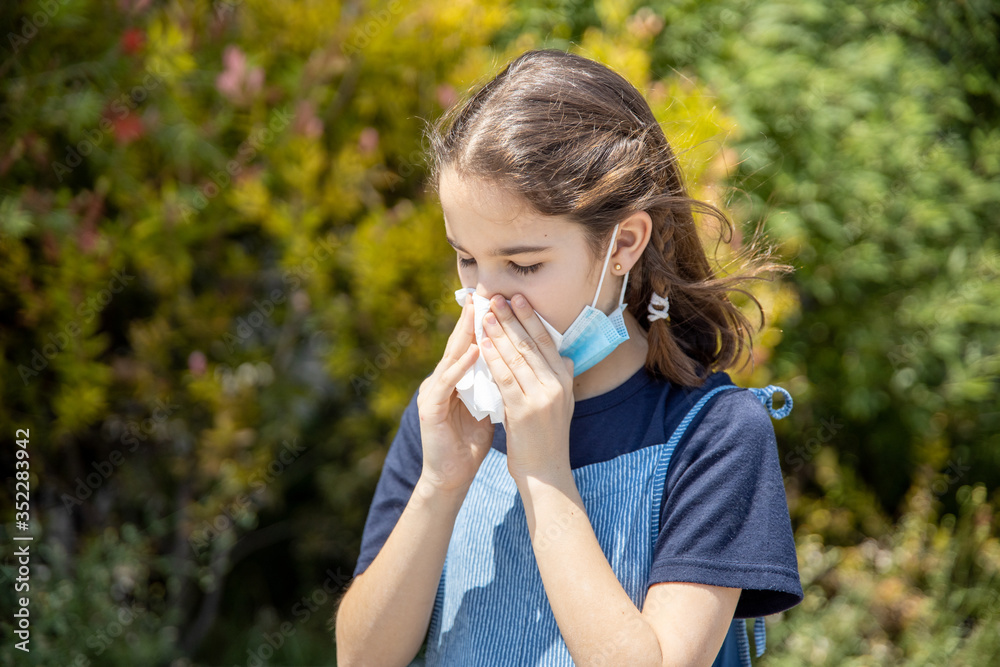 Sick little girl with allergy covering her mouth with a tissue in a park Sick little girl with allergy covering her mouth with a tissue in a park