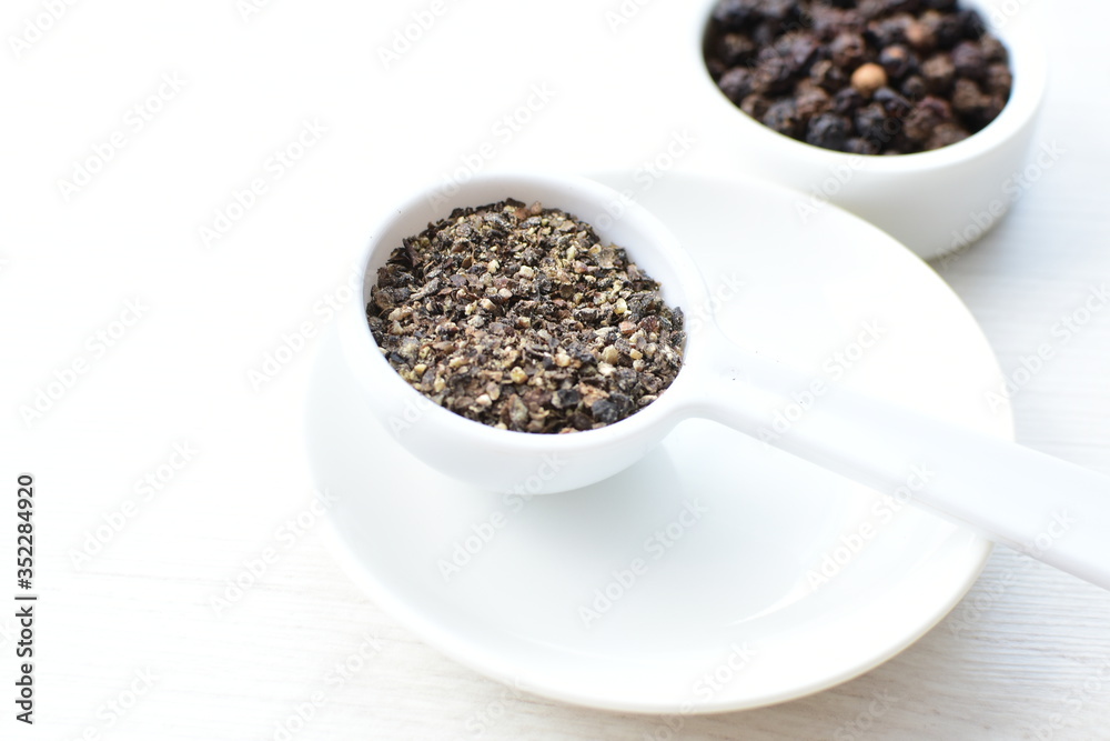 Whole and ground black peppercorns on white wooden background Whole and ground black peppercorns on white wooden background