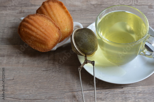 French madeline cakes next to a glass of green tea on a wooden table background