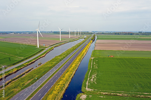 Aerial from a typical dutch landscape: Wind turbines, canals, straight roads and flat meadows in the countryside from the Netherlands