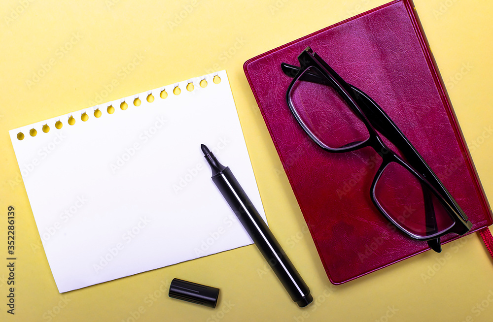 On a light background lies a burgundy diary, glasses and a sheet of paper on which you can write something On a light background lies a burgundy diary, glasses and a sheet of paper on which you can write something
