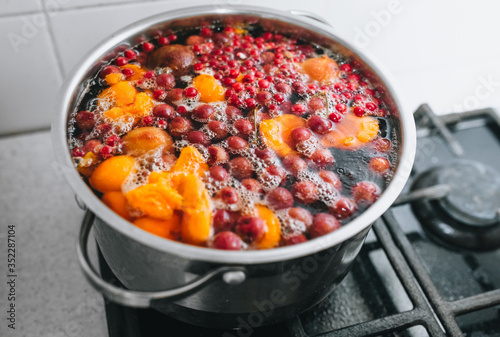 Fresh fruits are boiled in boiling water in a metal pan on the stove. Delicious stewed apricot, apples, cherries, raspberries. Photography, concept.