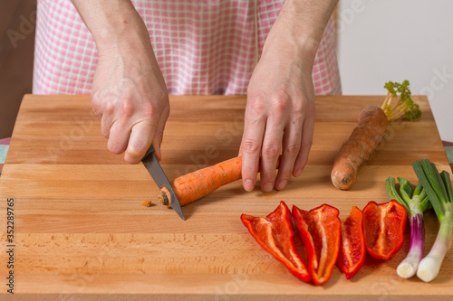 Close up of hands peeling and cutting carrots on a wooden board...Healthy food preparation concept