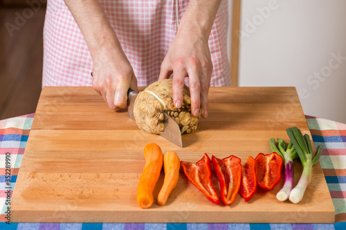 Close up of hands peeling and cutting celery root on a wooden board. Healthy food preparation concept