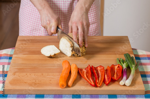 Close up of hands peeling and cutting celery root on a wooden board. Healthy food preparation concept